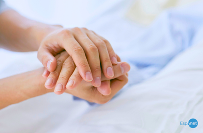 Close nas mãos de duas pessoas entrelaçadas em gesto de apoio e cuidado sobre uma cama hospitalar. No canto inferior direito, destaca-se o logotipo azul 'Espnet'