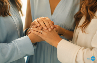 Três mulheres com vestidos claros unem as mãos em gesto de apoio e união, com foco nas mãos sobrepostas. No canto inferior direito, destaca-se o logotipo azul 'Espnet'