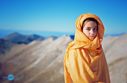 Menina afegã usando um lenço laranja sobre a cabeça, em frente a uma paisagem arida montanhosa sob um céu azul. No canto inferior esquerdo, destaca-se o logotipo azul 'Espnet'